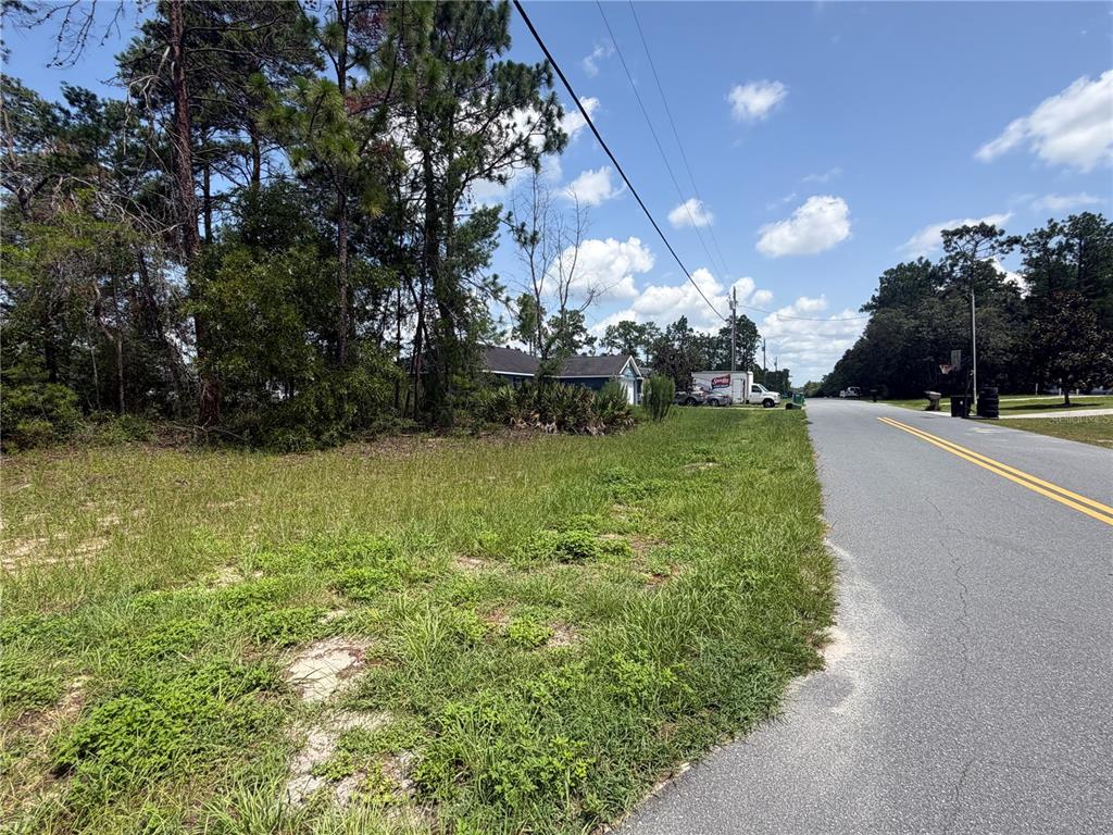 A grassy, undeveloped lot sits beside a paved road with trees and a house nearby — TBD SW 63RD TERRACE, OCALA, FL