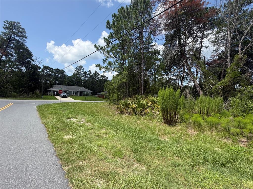 A grassy corner lot sits at a paved intersection near a house and trees — TBD SW 63RD TERRACE, OCALA, FL