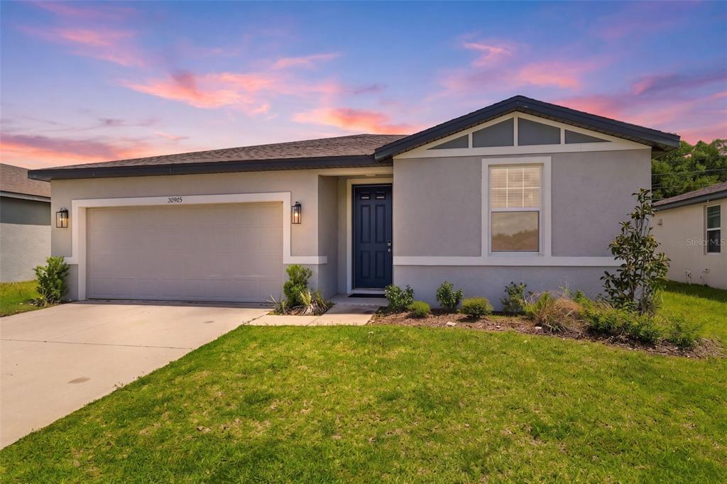 A single-story house with a gray stucco exterior, a two-car garage, and a dark door — 38905 HARLOW ROSE DRIVE, ZEPHYRHILLS, FL