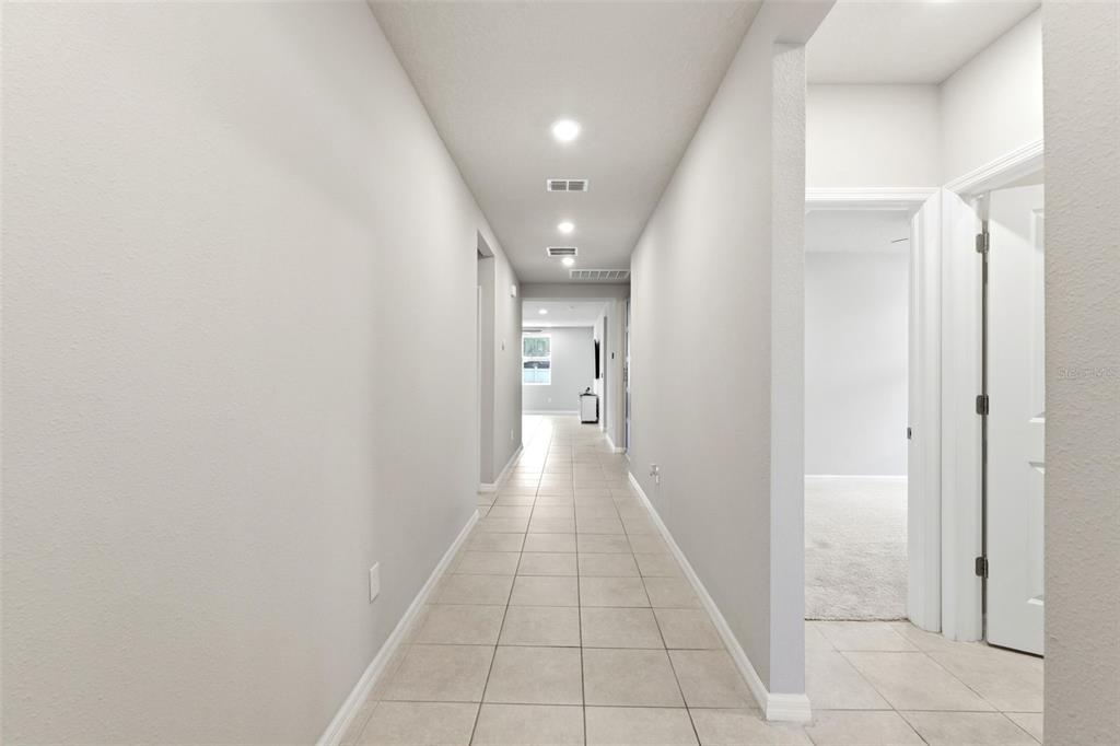 A long hallway with light-colored tile flooring leads toward a window at the far end — 38905 HARLOW ROSE DRIVE, ZEPHYRHILLS, FL