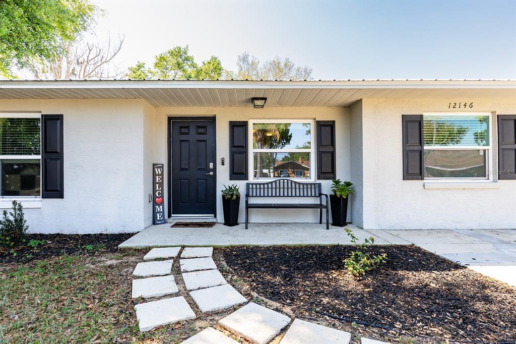 The exterior of a single-story house features a black front door, shutters, and a bench — 12146 VIRGINIA DRIVE, LEESBURG, FL