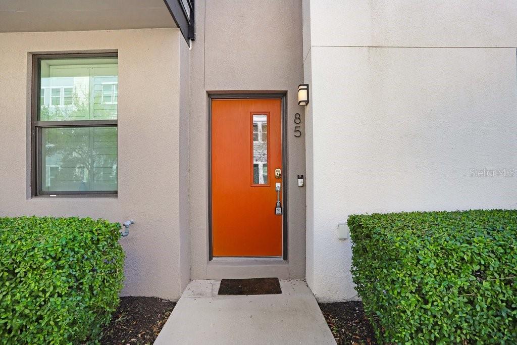 An orange front door with a vertical window is centered between two green bushes — 2511 N GRADY AVENUE UNIT 85, TAMPA, FL
