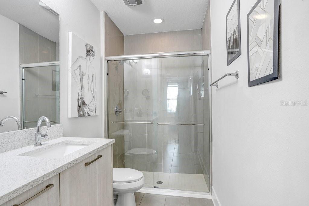 A bathroom features a light wood vanity, a glass-enclosed shower, and framed wall art — 2511 N GRADY AVENUE UNIT 85, TAMPA, FL