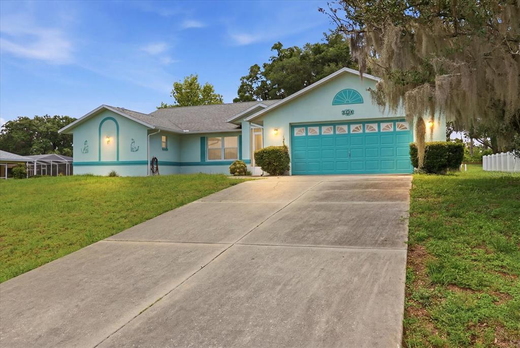 A light green single-story house features a teal garage door and a concrete driveway — 1209 N TIMUCUAN TRAIL, INVERNESS, FL