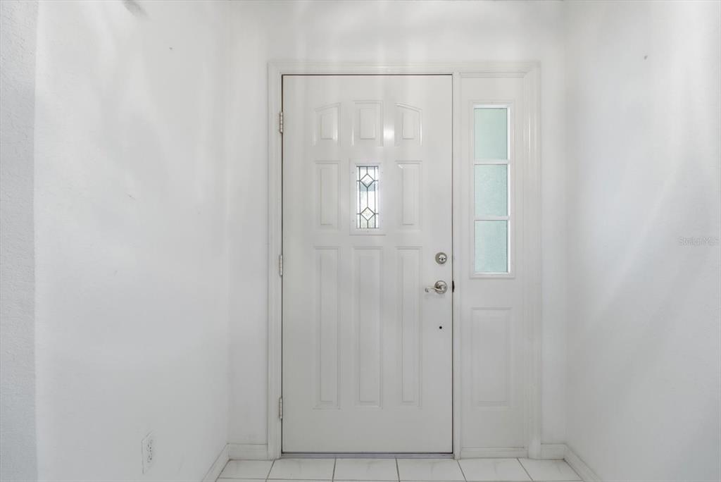 A white front door with a glass insert and sidelight sits in a tiled entryway — 1209 N TIMUCUAN TRAIL, INVERNESS, FL