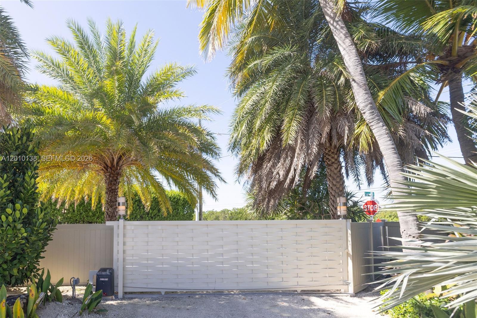 A white horizontal-slat gate stands between two palm trees in front of a fence — 74049 Overseas, Islamorada FL 33036, ISLAMORADA, FL