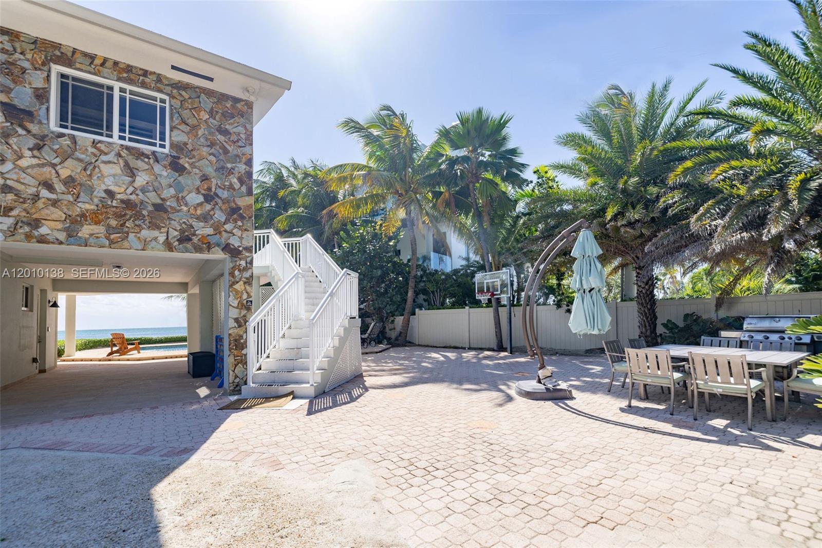A paved patio features a dining set, basketball hoop, and stairs leading to a stone house — 74049 Overseas, Islamorada FL 33036, ISLAMORADA, FL