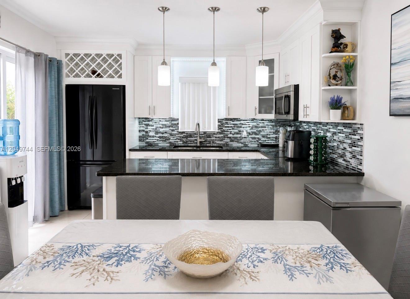 A kitchen features white cabinets, black countertops, a mosaic backsplash, and a dining area — 4804 Waterview Cir, Palm Springs FL 33461, PALM SPRINGS, FL