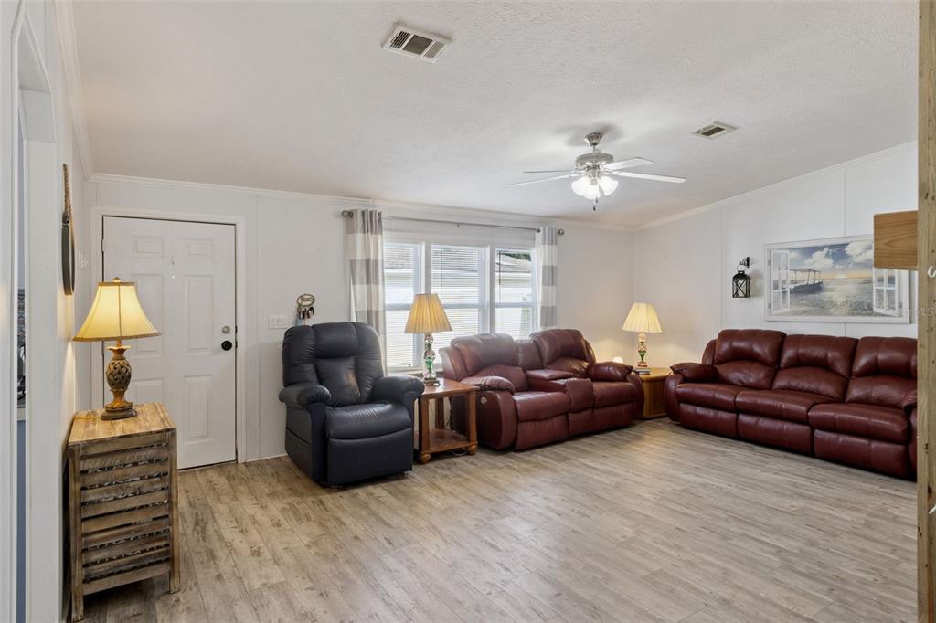 A living room features light wood-look flooring, white walls, a ceiling fan, and leather furniture — 3100 MARK LANE, LAKE WALES, FL