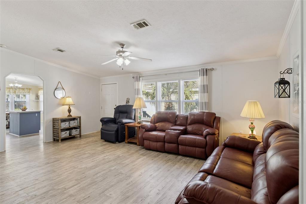 A living room features light wood-look flooring, brown leather furniture, and a ceiling fan — 3100 MARK LANE, LAKE WALES, FL