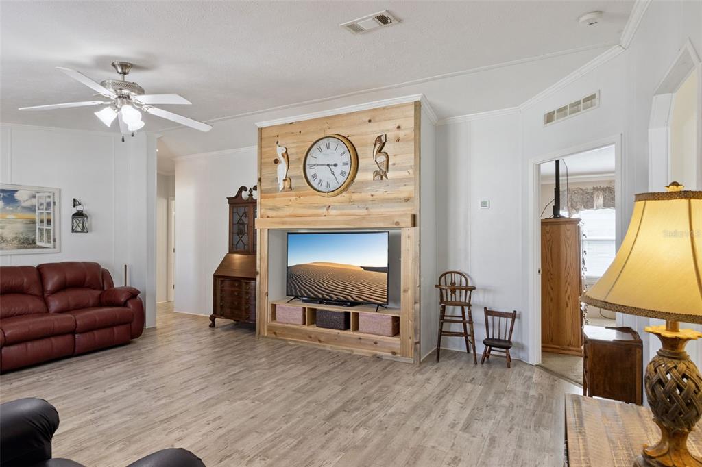A living room features a wood-paneled accent wall with a television and a large clock — 3100 MARK LANE, LAKE WALES, FL