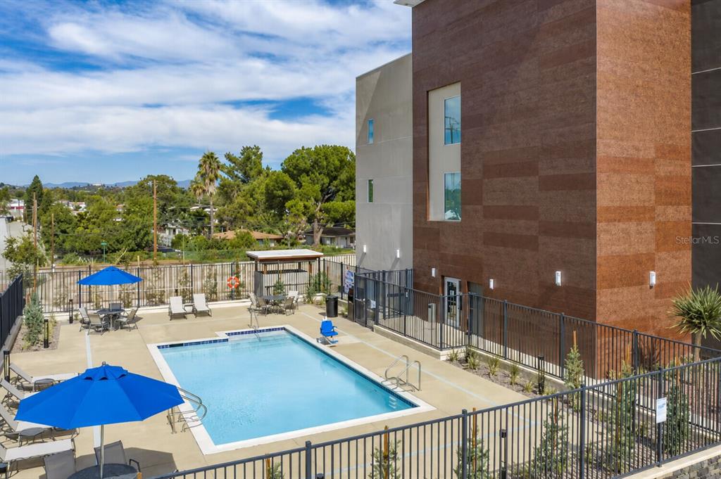 An outdoor swimming pool with blue umbrellas and lounge chairs sits beside a modern building — 22417 HANCOCK AVENUE, PUNTA GORDA, FL