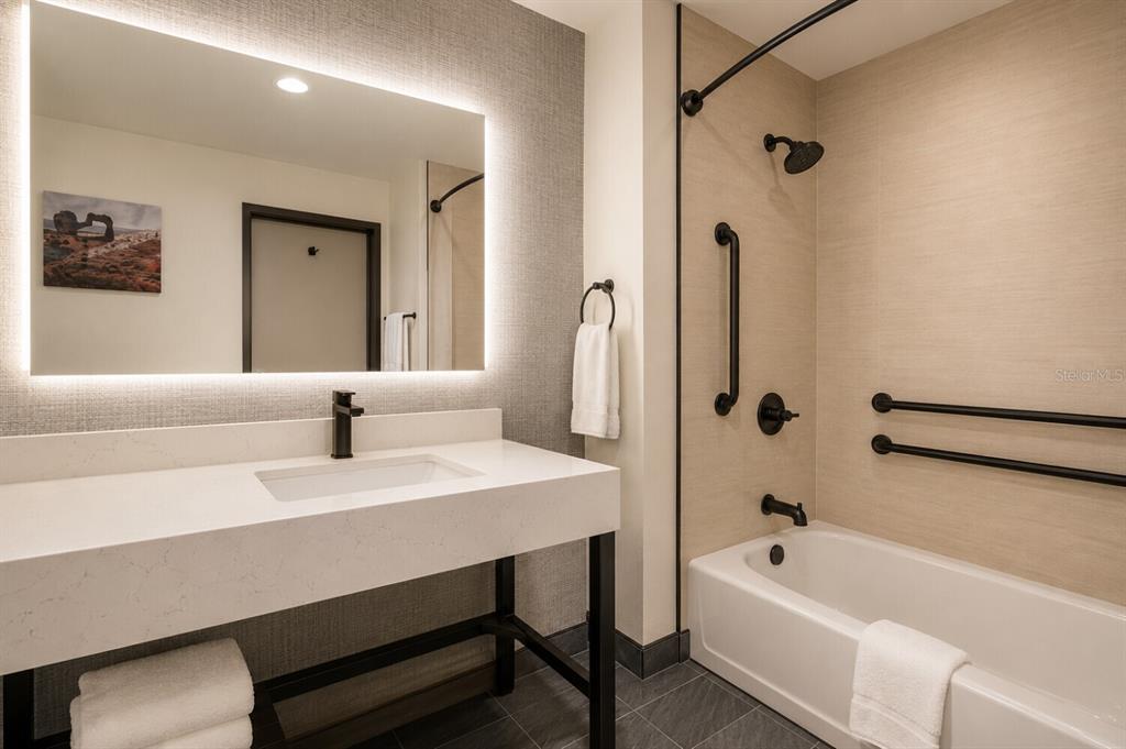A modern bathroom features a white vanity, a backlit mirror, and a tub-shower combination — 22417 HANCOCK AVENUE, PUNTA GORDA, FL