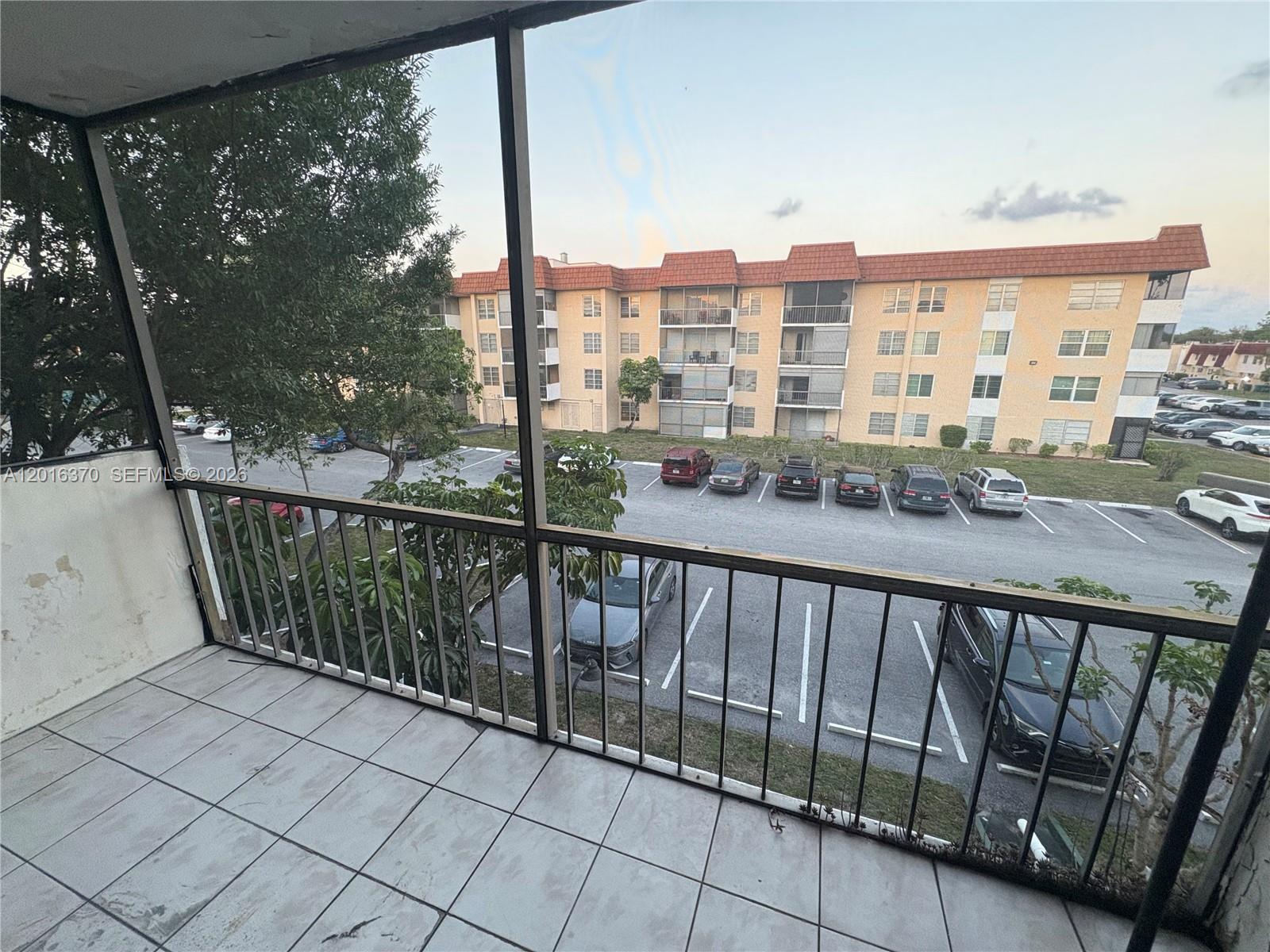 A tiled balcony with a metal railing overlooks a parking lot and an apartment building — 4152 Inverrary Dr # 303, Lauderhill FL 33319, LAUDERHILL, FL