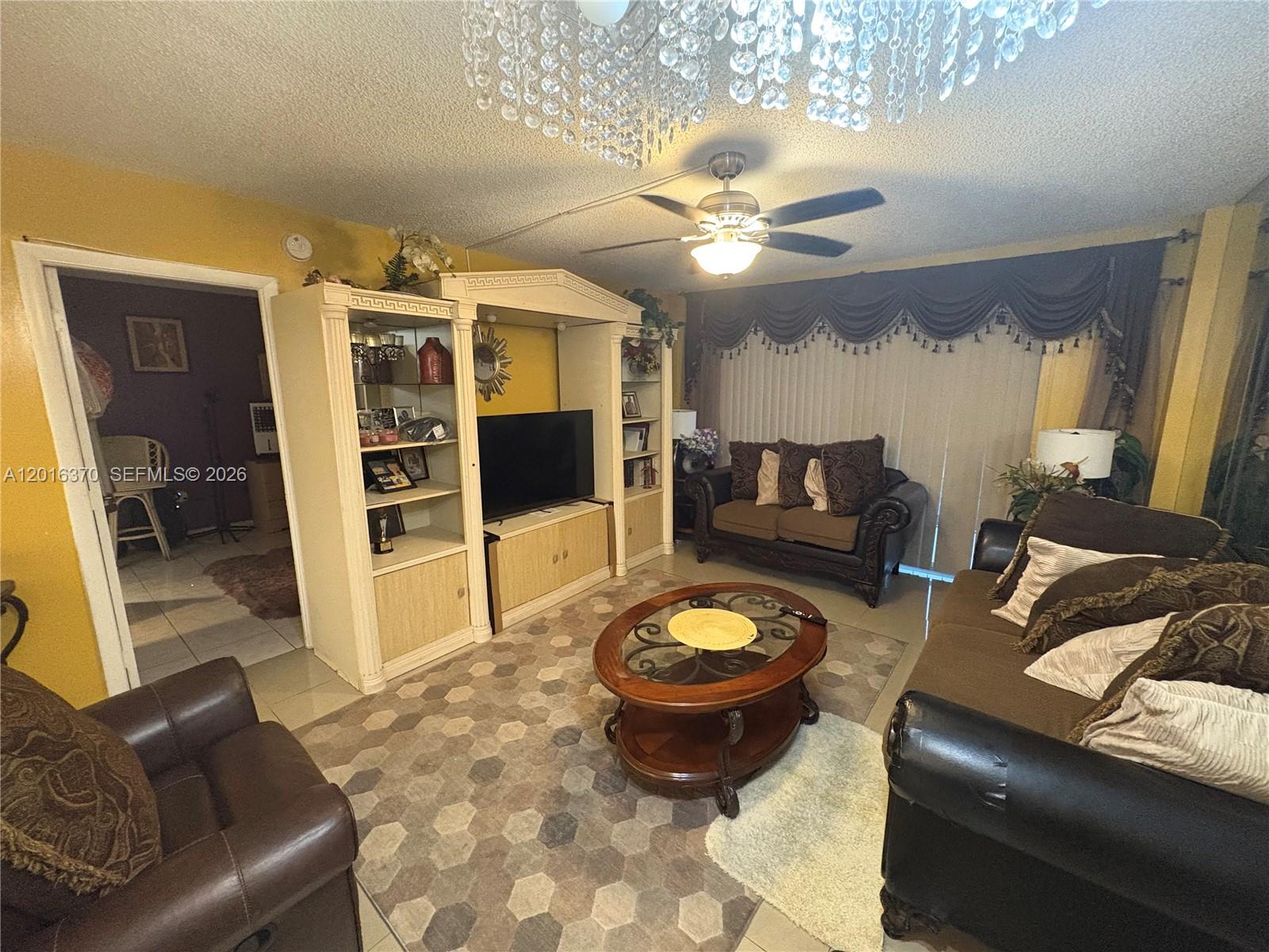 A living room features a large entertainment center, brown leather sofas, and a crystal chandelier — 4152 Inverrary Dr # 303, Lauderhill FL 33319, LAUDERHILL, FL