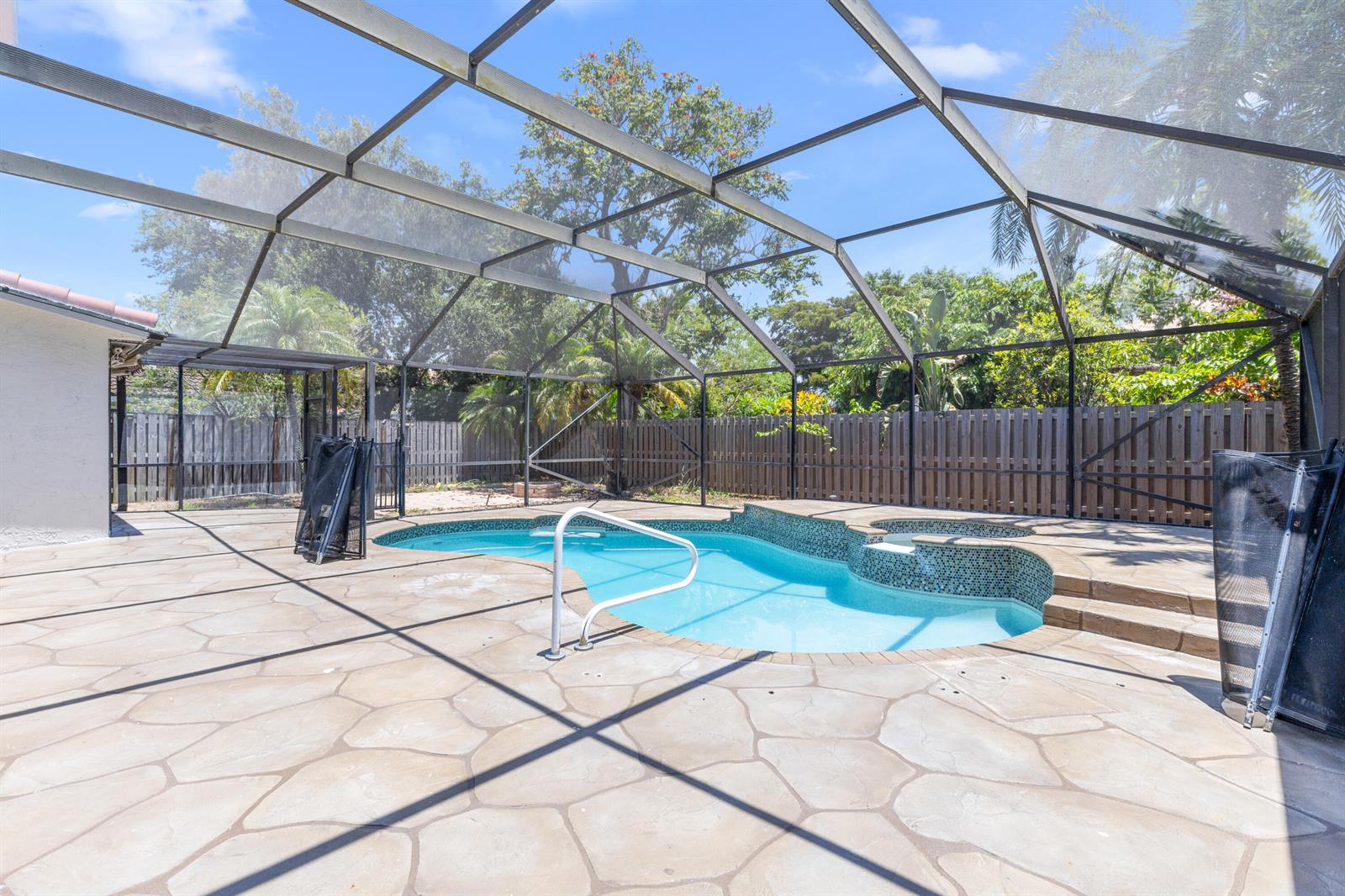 A swimming pool with a spa and a white handrail sits inside a screened enclosure — 7686 Cedar Hurst Court, Lake Worth FL 33467, LAKE WORTH, FL