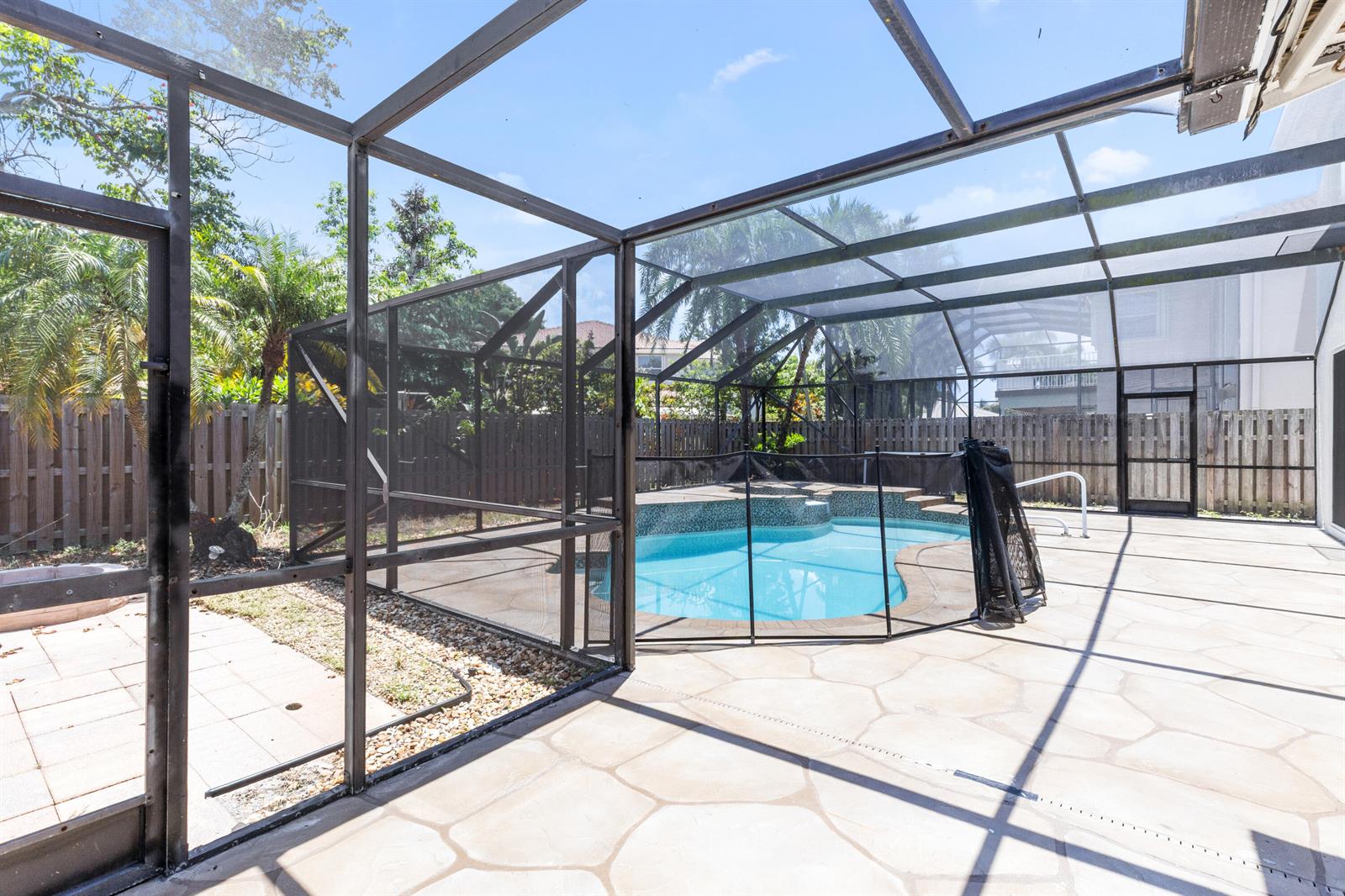 A screened-in patio features a swimming pool with a safety fence and stone-patterned pavers — 7686 Cedar Hurst Court, Lake Worth FL 33467, LAKE WORTH, FL