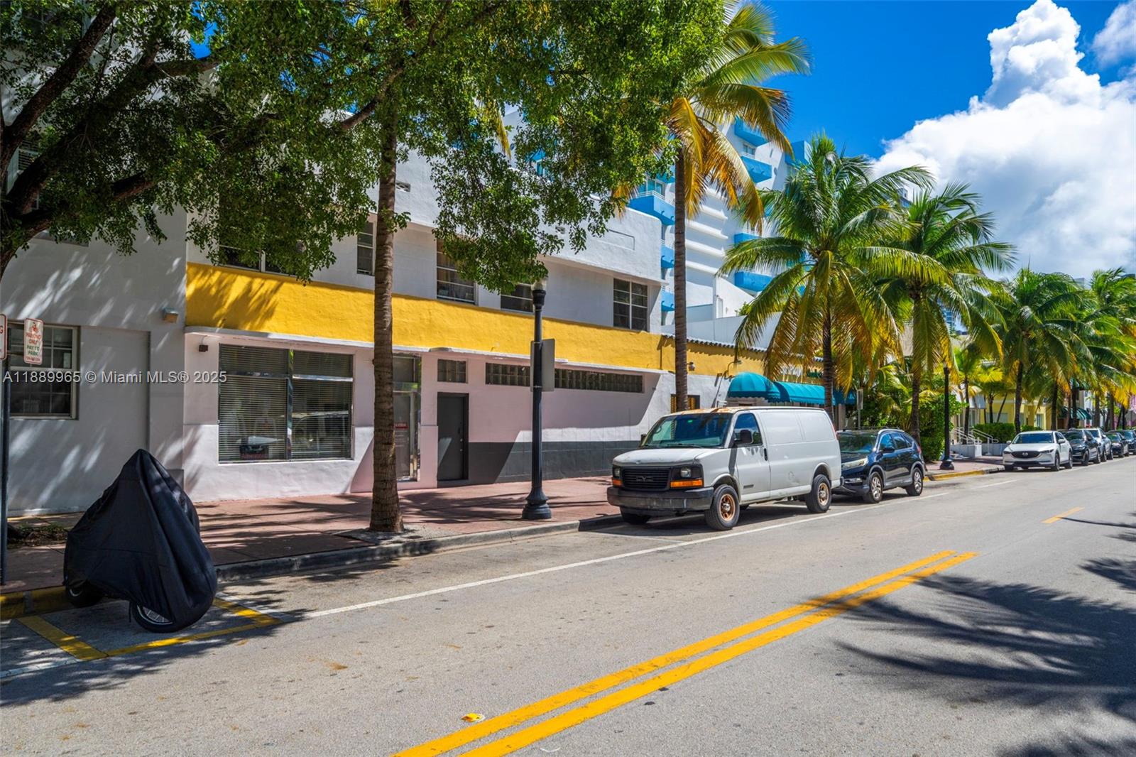 A white building with a yellow accent stripe stands along a street with parked vehicles — 249 Collins Ave, Miami Beach FL 33139, MIAMI BEACH, FL