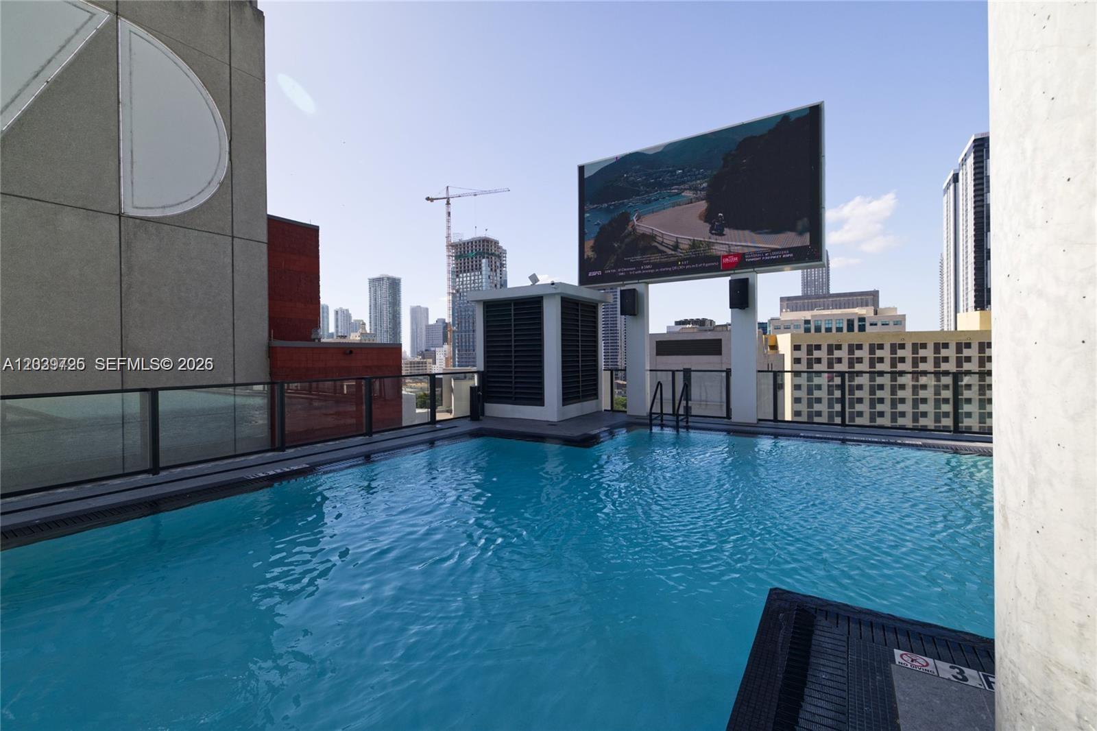 A rooftop swimming pool overlooks a city skyline with a large outdoor television screen — 398 NE 5th St # 2112, Miami FL 33132, MIAMI, FL