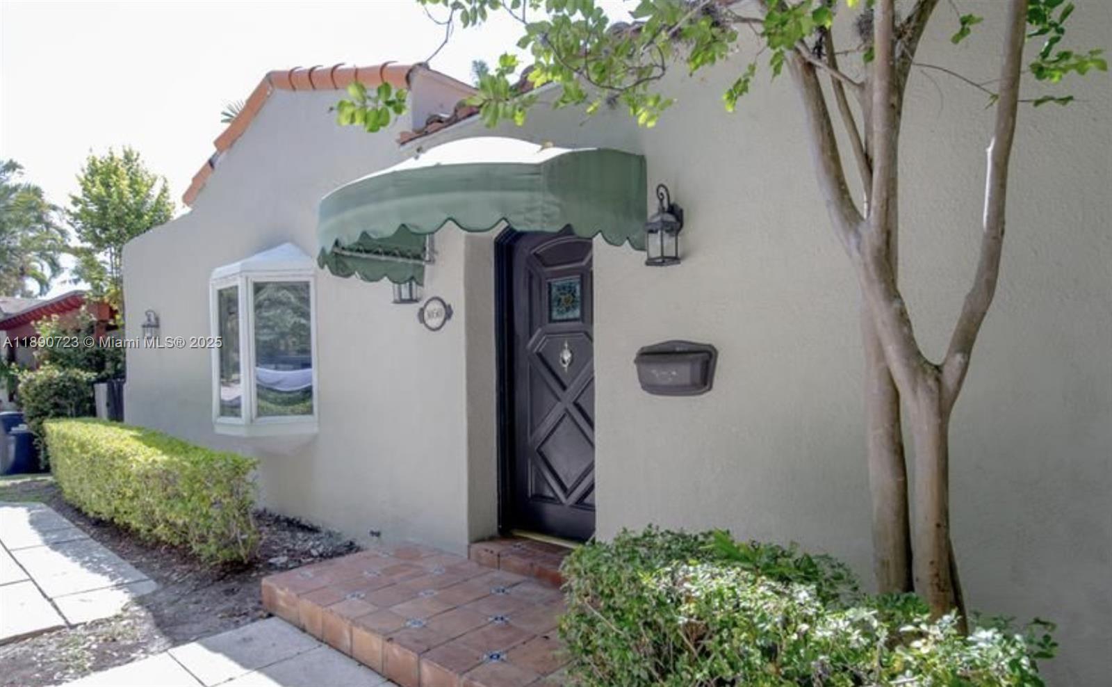 The exterior of a house features a tiled entryway, a green awning, and a dark door — 3050 Alton Rd, Miami Beach FL 33140, MIAMI BEACH, FL