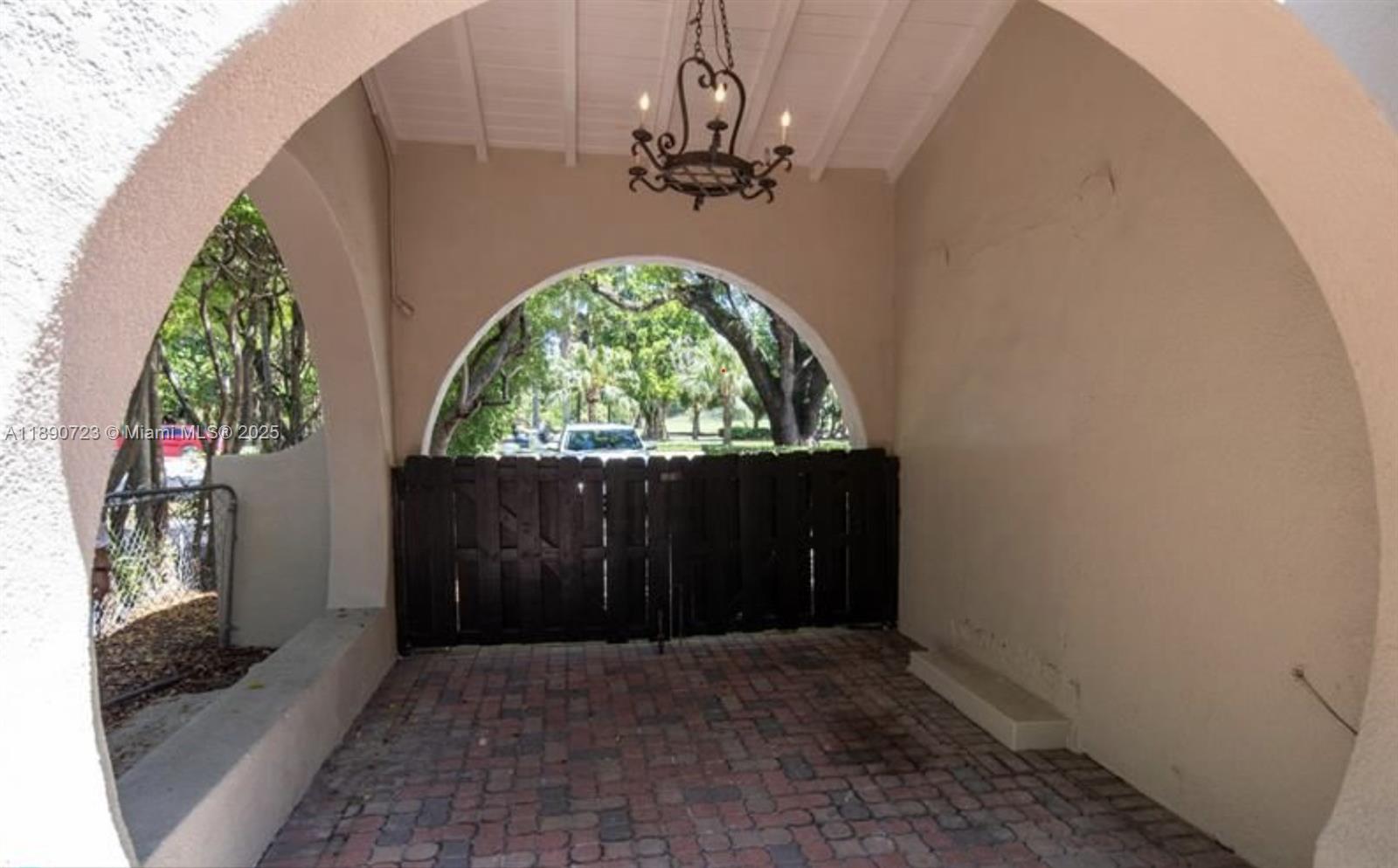 A covered brick patio features a large arched entryway, a wooden gate, and a chandelier — 3050 Alton Rd, Miami Beach FL 33140, MIAMI BEACH, FL