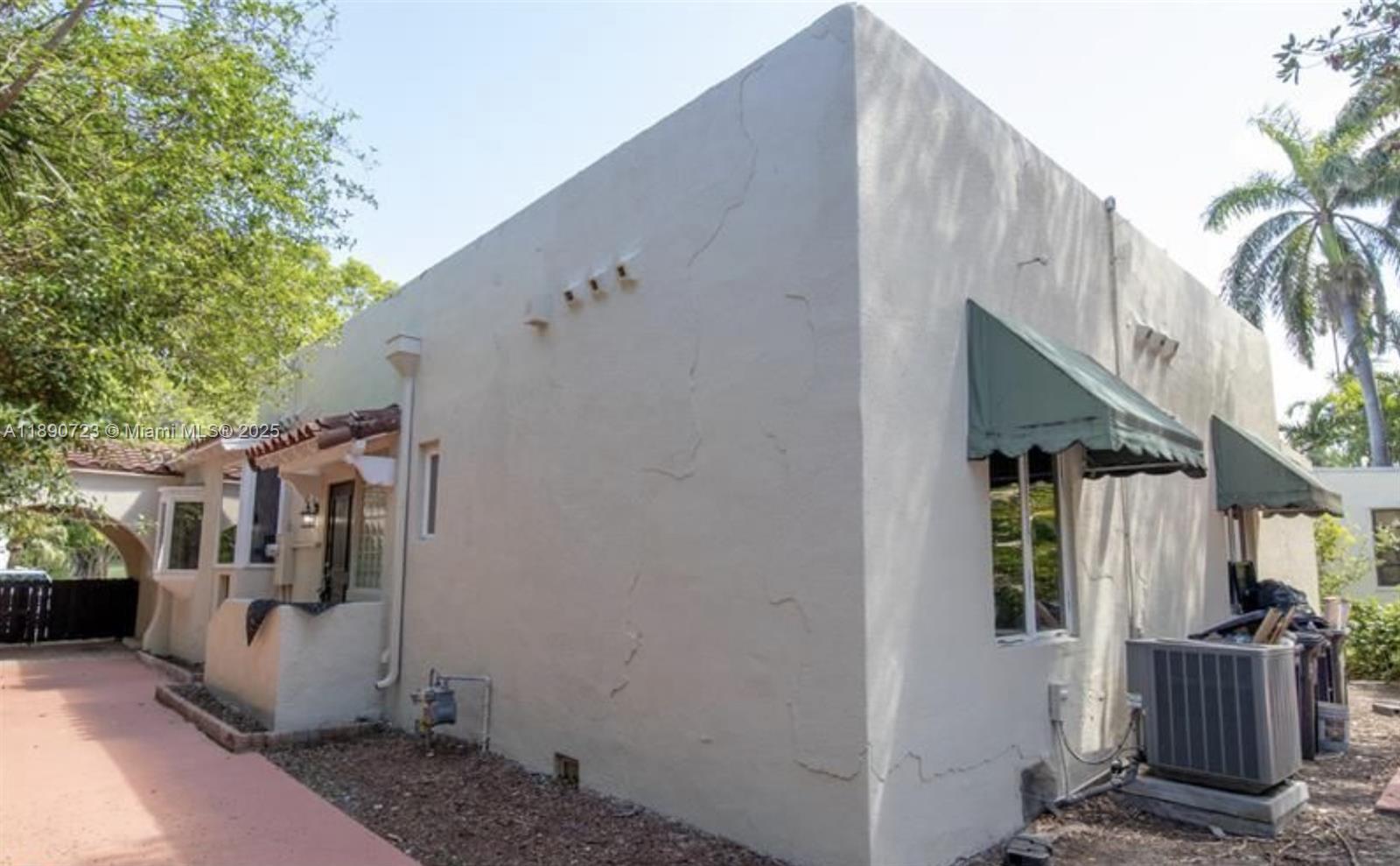 The exterior of a stucco house features green awnings, a side entrance, and an air conditioner — 3050 Alton Rd, Miami Beach FL 33140, MIAMI BEACH, FL