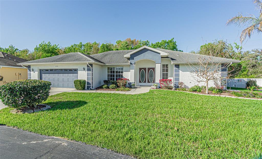 A single-story suburban house features a two-car garage, a central entryway, and a grassy lawn — 10504 MOSHIE LANE, SAN ANTONIO, FL