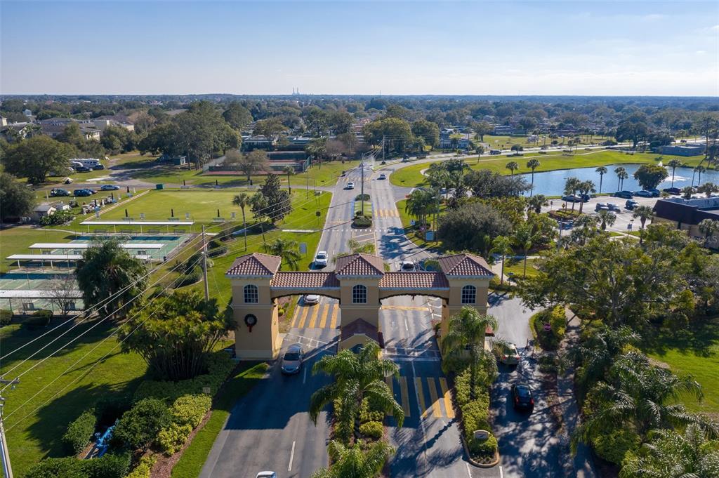 An aerial view shows a gated entrance with three stone towers over a paved road — 1609 LAUGHTON PLACE, SUN CITY CENTER, FL