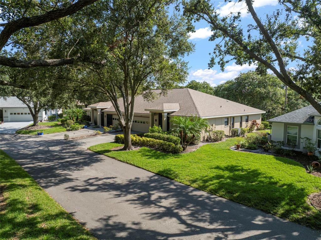 A tan single-story house with a shingled roof and a paved driveway under large trees — 1609 LAUGHTON PLACE, SUN CITY CENTER, FL