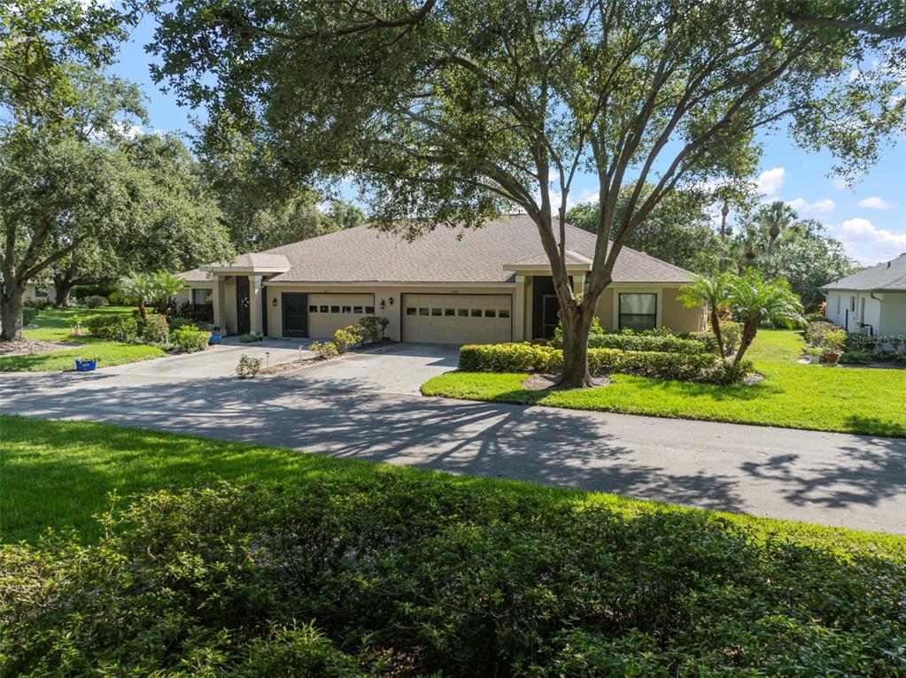 A duplex with two garage doors and a shared driveway sits under large shade trees — 1609 LAUGHTON PLACE, SUN CITY CENTER, FL
