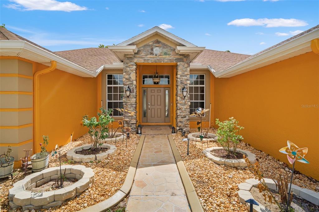 The exterior of a house features an orange stucco facade, stone entryway, and gravel landscaping — 14188 DORADO STREET, SPRING HILL, FL