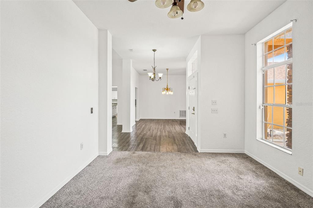A room with gray carpet leads to a dining area with wood-look flooring and chandeliers — 14188 DORADO STREET, SPRING HILL, FL
