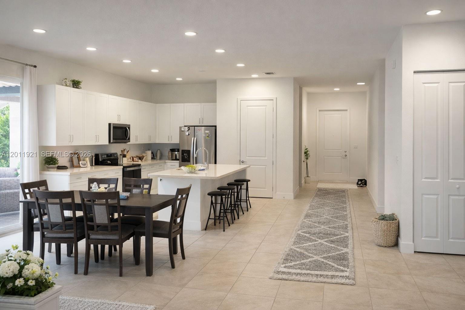 A modern kitchen features white cabinetry, a central island with bar stools, and an adjacent dining area — 4993 OFANTO LN, Ave Maria FL 34142, AVE MARIA, FL