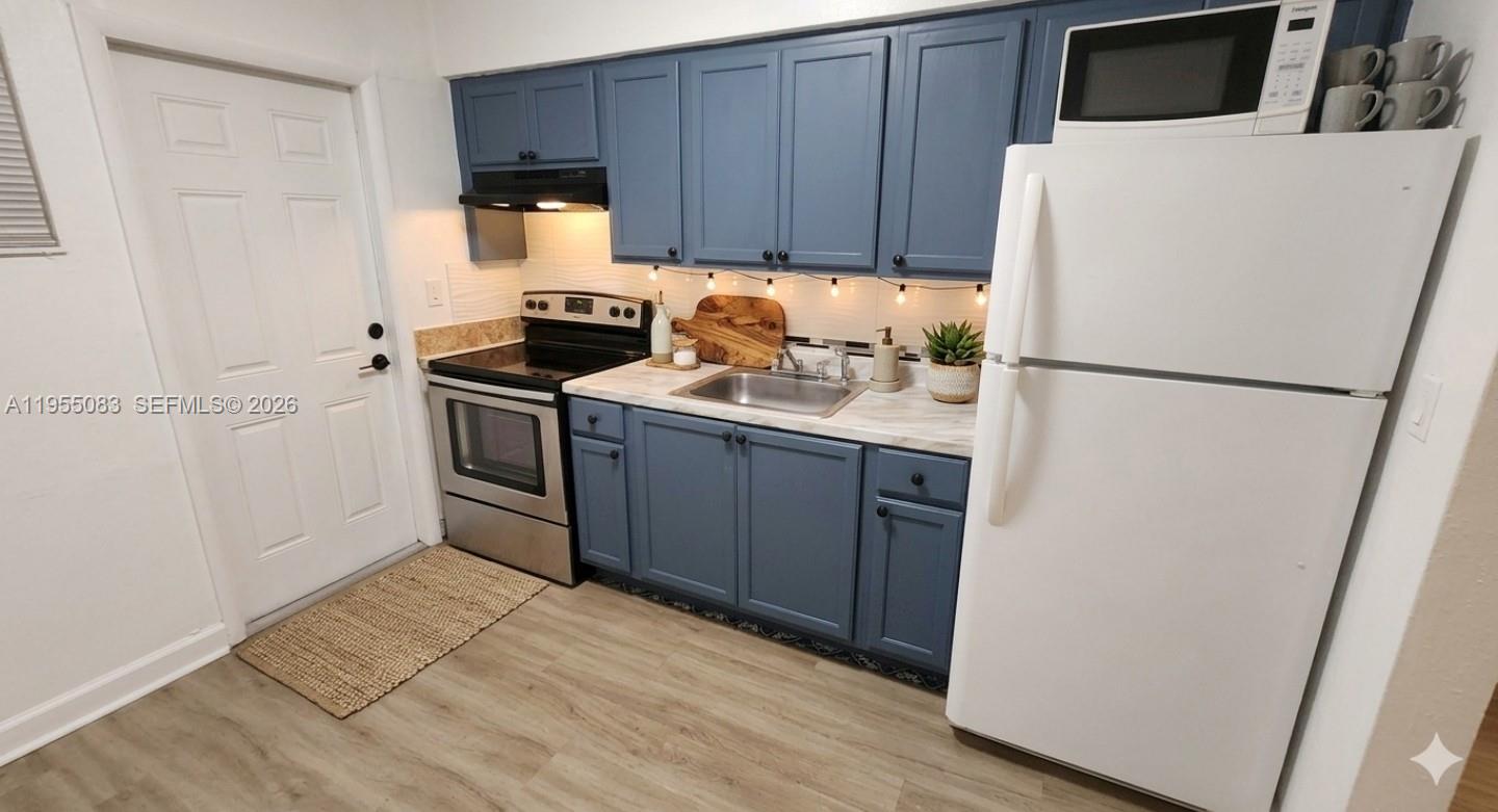 A small kitchen features gray wood-look flooring, white walls, and a white exterior door — 2729 NW 47th St, Miami FL 33142, MIAMI, FL