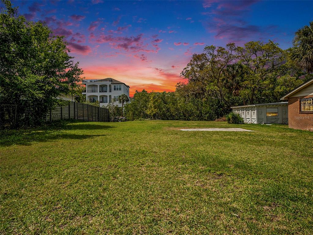 A grassy backyard features a concrete pad, a wooden fence, and a nearby multi-story house — 7406 BAY DRIVE, TAMPA, FL