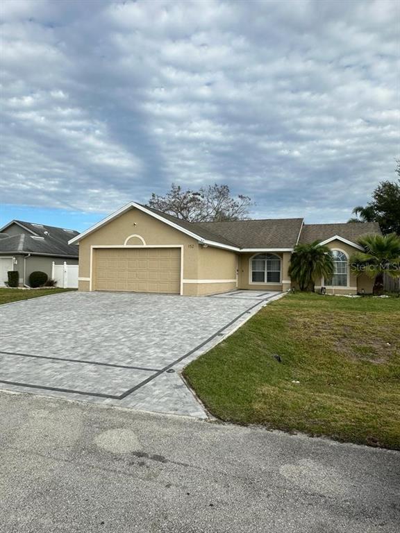 A single-story house with a tan stucco exterior, a paved driveway, and a two-car garage — 152 WHITEHALL STREET, DAVENPORT, FL