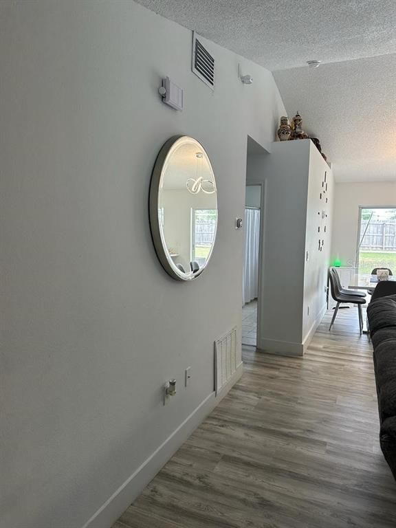 A hallway with light wood-look flooring leads toward a dining area with a round mirror — 152 WHITEHALL STREET, DAVENPORT, FL