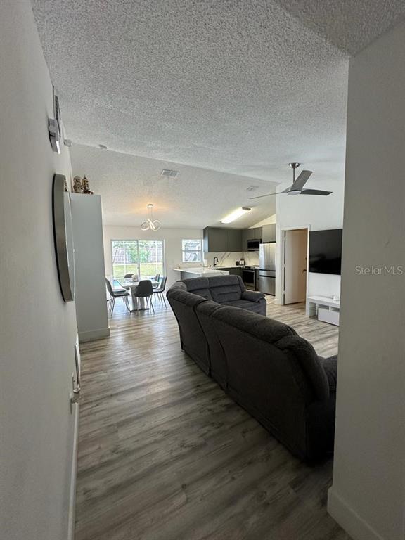 An open-concept living and dining area features wood-look flooring, a gray sofa, and a kitchen — 152 WHITEHALL STREET, DAVENPORT, FL