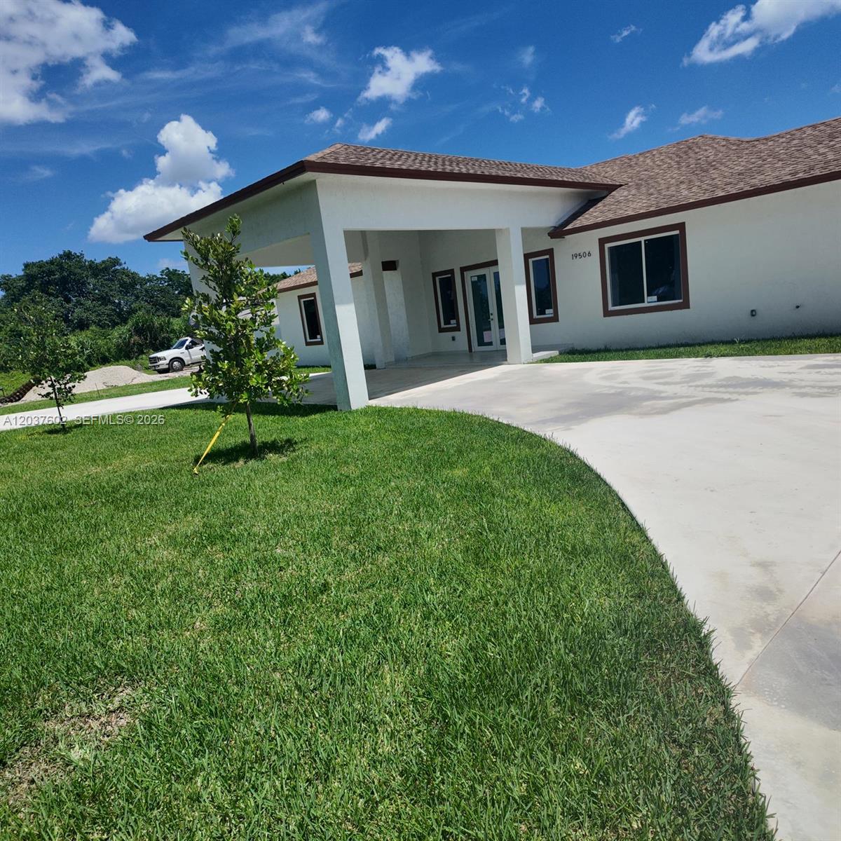 A single-story house with a covered entryway, brown roof, and a large concrete driveway — HOMESTEAD, FL