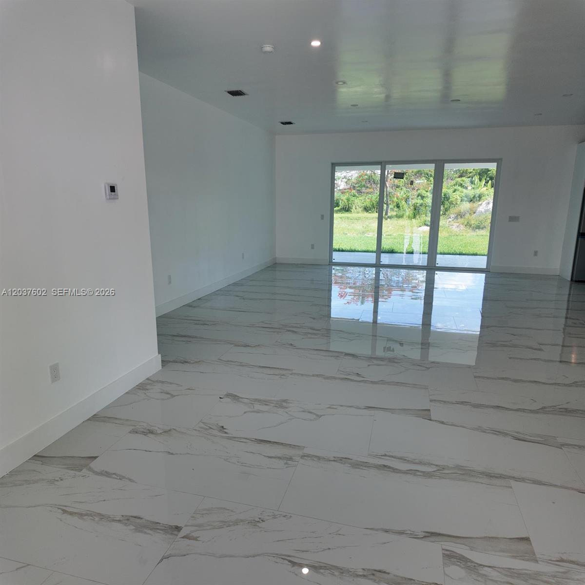 An empty room features white walls, large marble-patterned floor tiles, and sliding glass doors — HOMESTEAD, FL