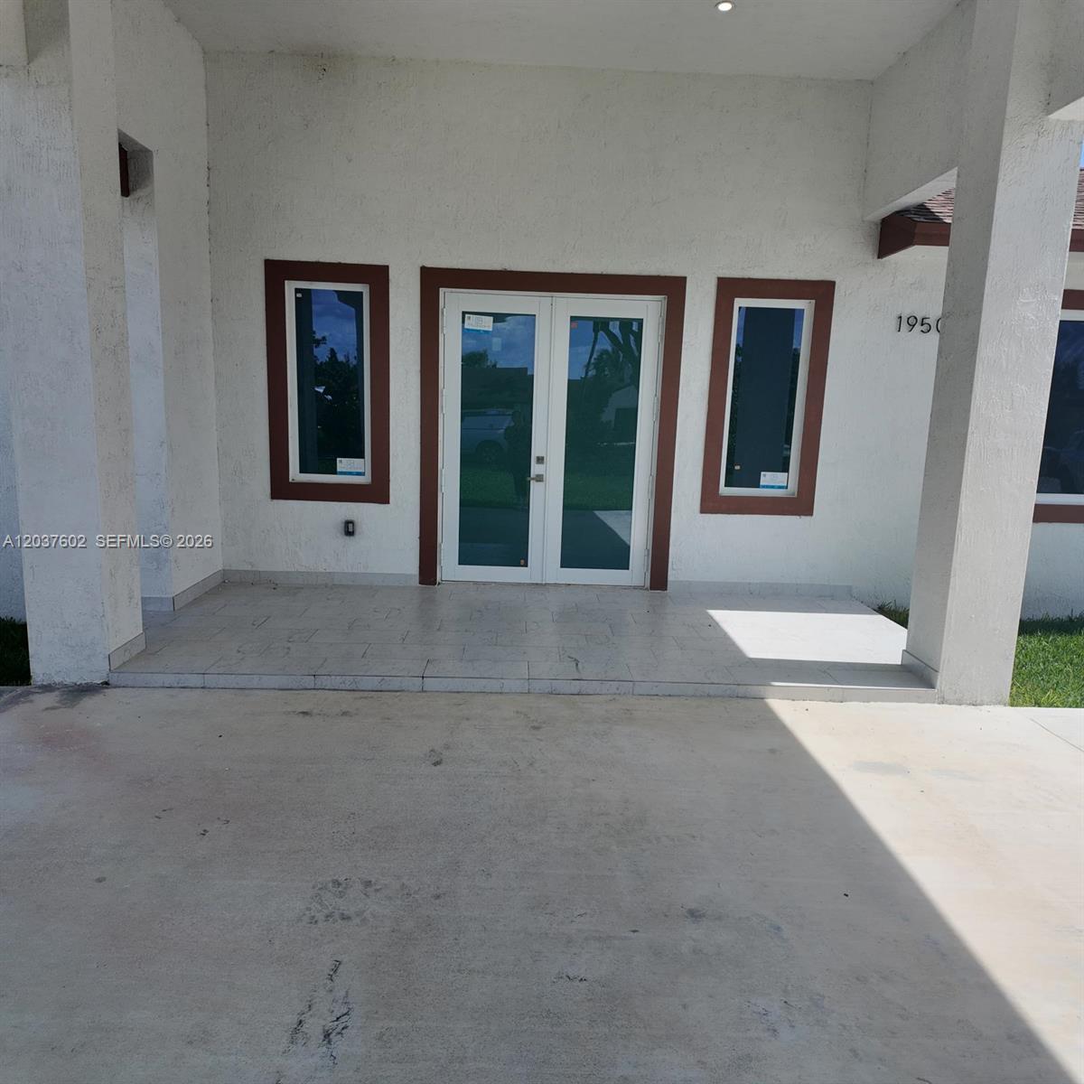 A covered concrete porch features a double glass door flanked by two narrow windows — HOMESTEAD, FL