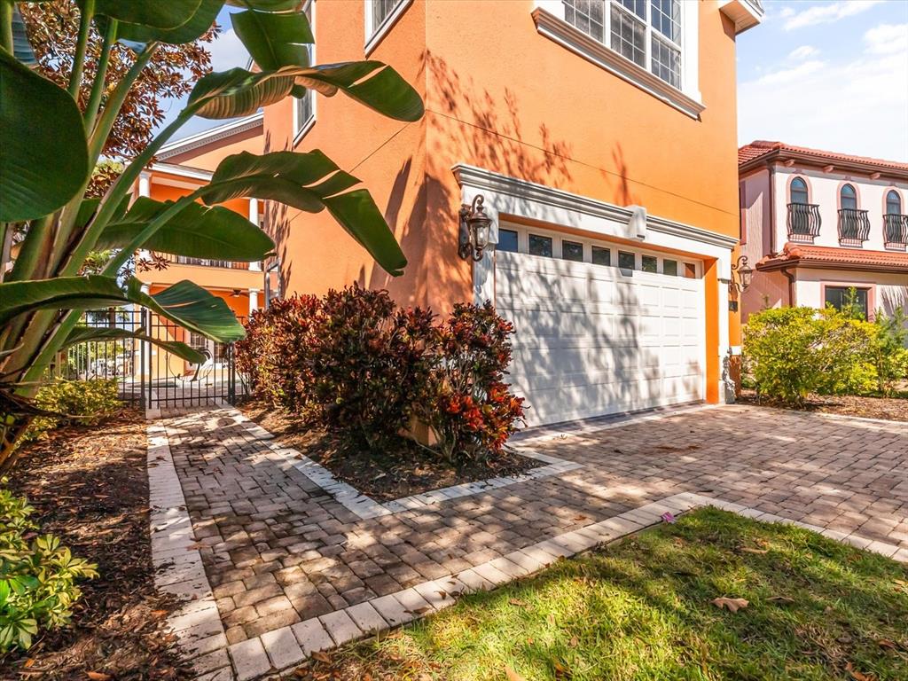 An orange house features a white garage door, a brick paver driveway, and landscaped bushes — 1554 COROLLA COURT, REUNION, FL