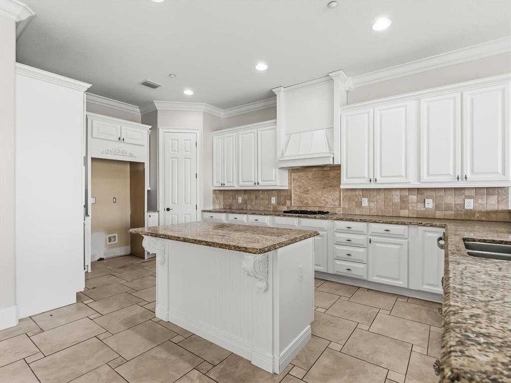 A kitchen features white cabinets, a granite-topped island, tile flooring, and a tiled backsplash — 1554 COROLLA COURT, REUNION, FL