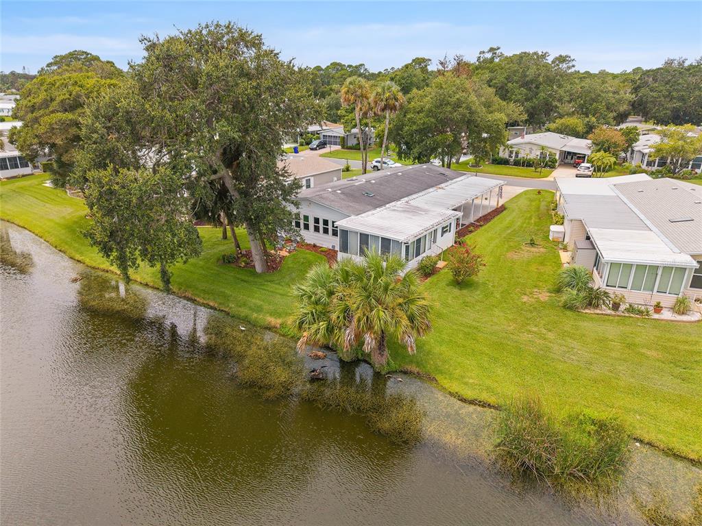 An aerial view shows a manufactured home with a screened porch situated beside a pond — 621 STARBOARD AVENUE, EDGEWATER, FL