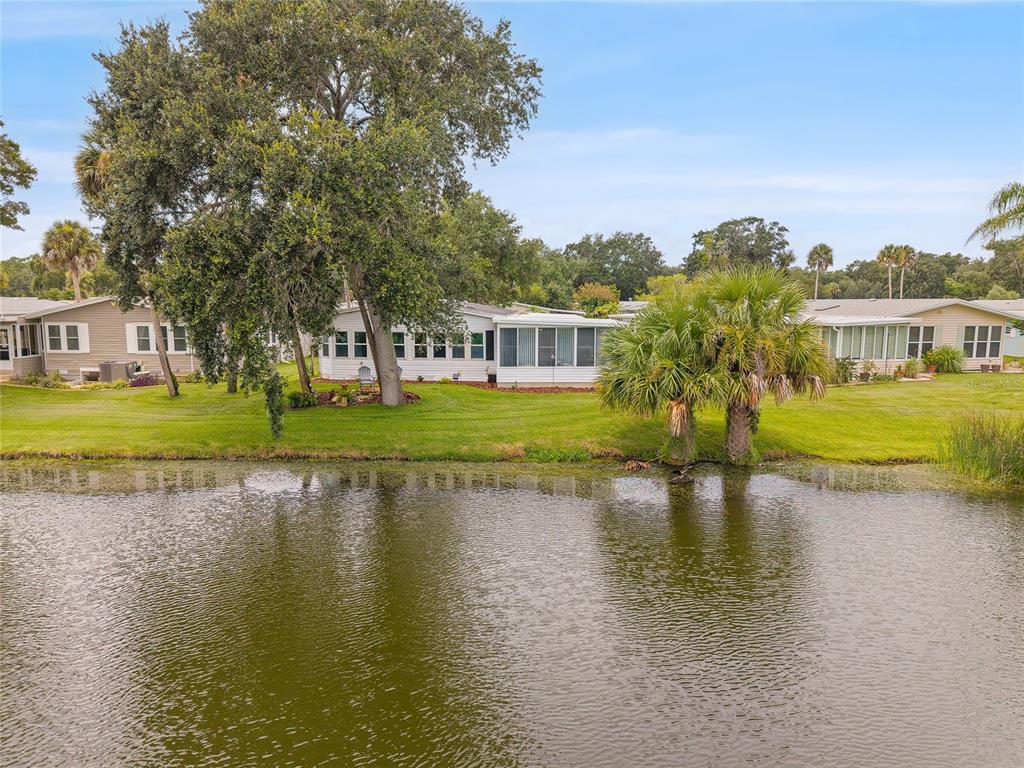 A view of a pond with several manufactured homes and large trees in the background — 621 STARBOARD AVENUE, EDGEWATER, FL