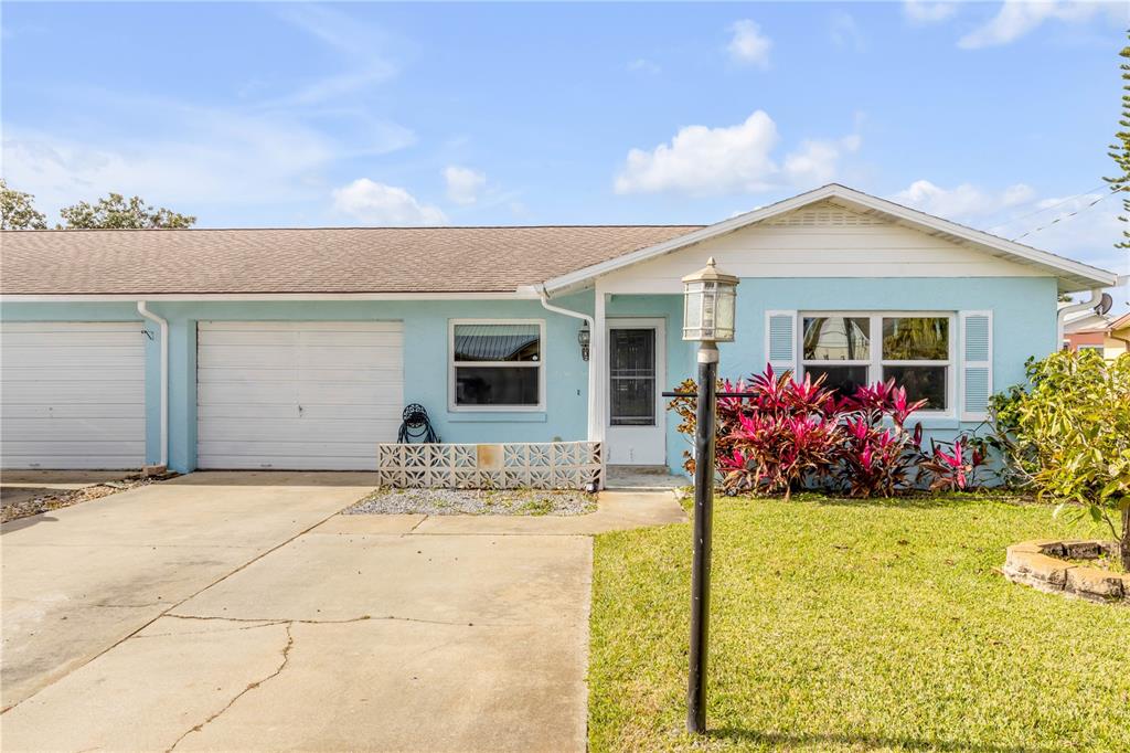 A light blue single-story house features a white garage, a front door, and landscaping — 26 LAUGHING GULL LANE, EDGEWATER, FL