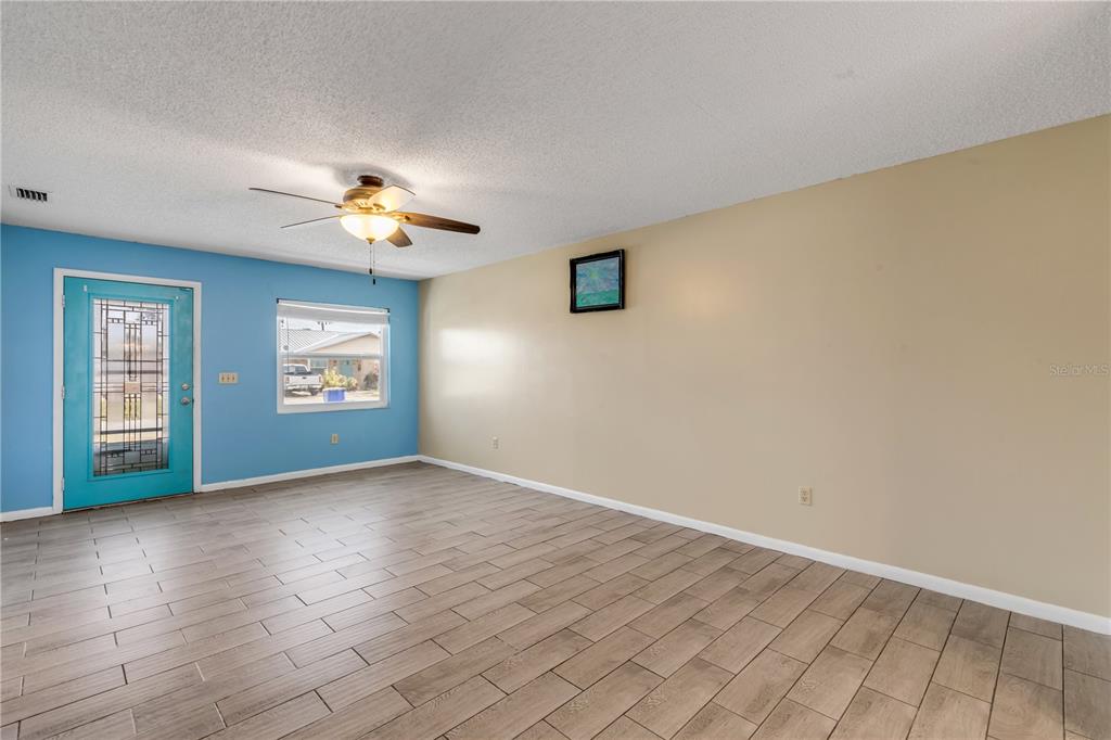 A living room features light blue and beige walls, wood-look tile flooring, and a ceiling fan — 26 LAUGHING GULL LANE, EDGEWATER, FL