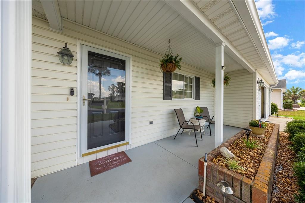 A covered front porch features light siding, a brick planter, and two chairs — 14748 SW 112TH CIRCLE, DUNNELLON, FL