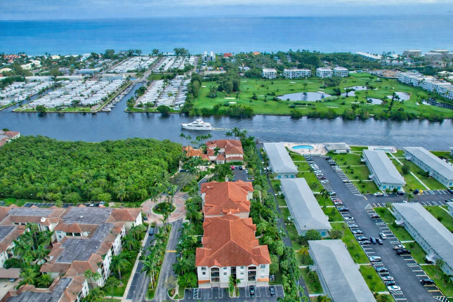 Aerial view of a waterfront residential complex with a canal, boat, and golf course nearby — 1306 Tuscany Way # 306, Boynton Beach FL 33435, BOYNTON BEACH, FL