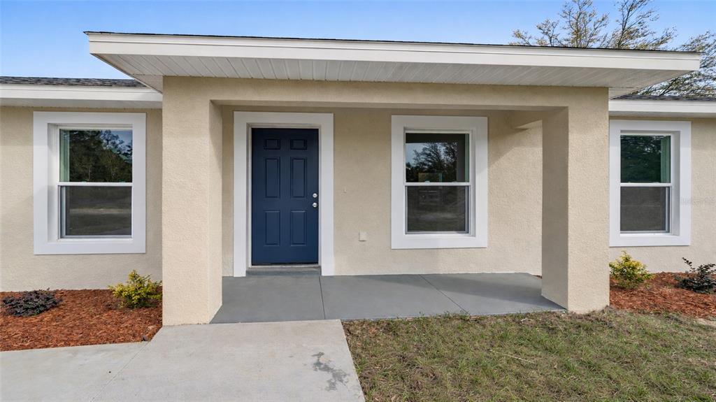 The exterior of a house features a blue front door, white trim, and a concrete porch — 15350 SW 38TH PLACE, OCALA, FL